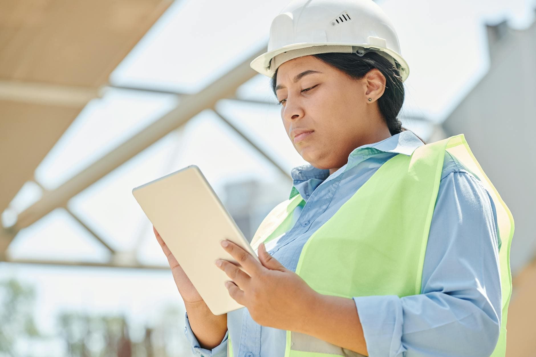 A worker in a hard hat logging information on a tablet at a worksite.