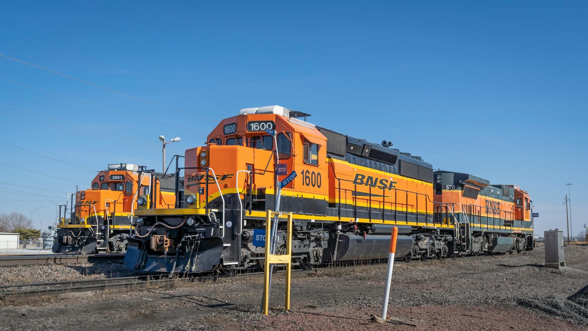Three orange BNSF locomotives parked on the tracks under a clear blue sky.