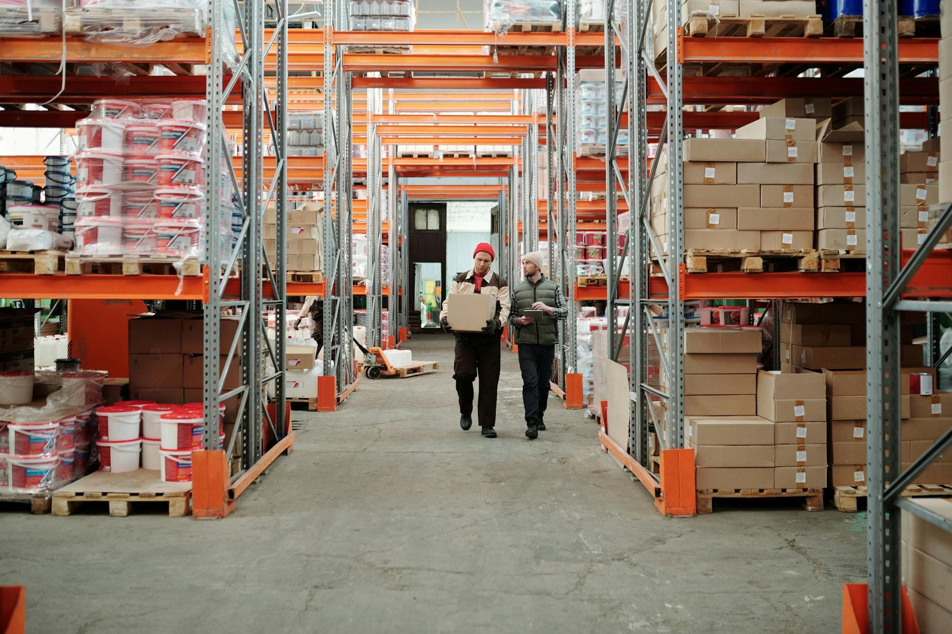 Two workers handling a package in a large distribution warehouse aisle.